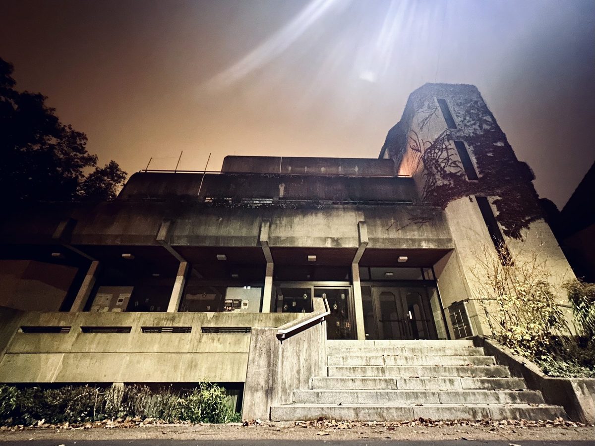 Betonbau mit Treppe und efeubewachsenem Turm, nachts von unten fotografiert