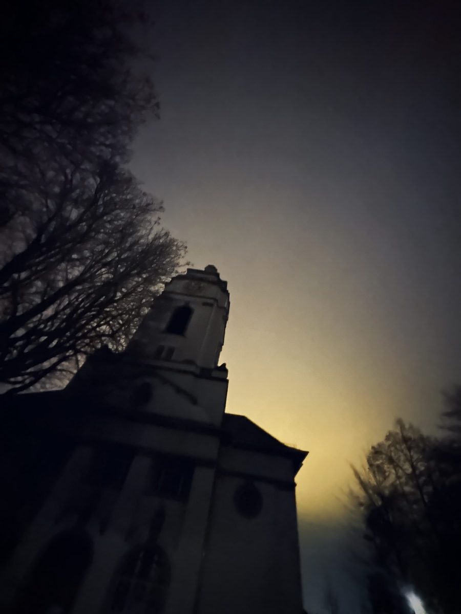 Silhouette eines Kirchturms zwischen kahlen Bäumen im nächtlichen Nebel